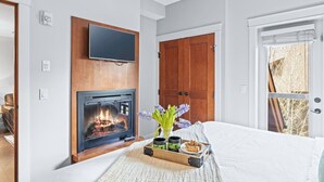 Een slaapkamer met een open haard, een televisie, een houten deur en een raam.