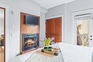 A bedroom with a fireplace, a television, a wooden door, and a window. - Lovely 2BR Rockies Getaway w Pool + Hot Tub Access (Canmore)