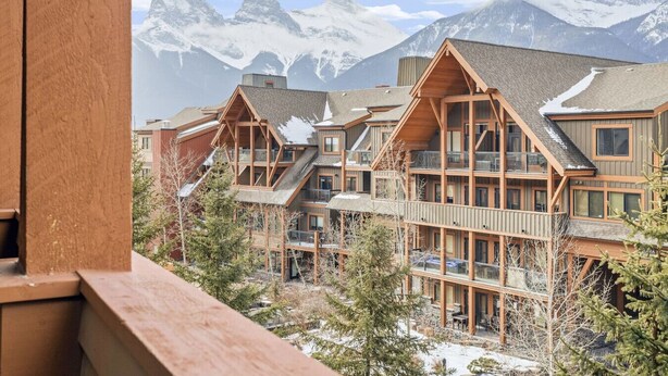 Een meerlaags landhuis met houten balkons en een bergachtige achtergrond.