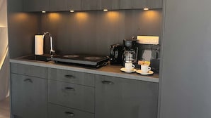A kitchenette with a stove, coffee maker, and two cups on the counter.