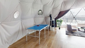 A tented room with a ping pong table, a fireplace, and a view through a large window.