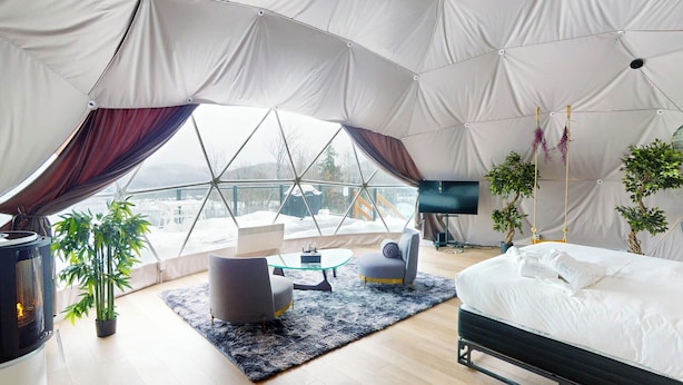 A spacious tented room with a bed, seating area, and a TV.