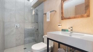 A modern bathroom with a glass shower enclosure, a white toilet, and a large vanity with a mirror. - Bel Air Tremblant CALAFATE : 1 CHAMBRE, JACUZZI, SAUNA (La Conception)