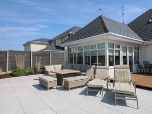 A covered patio with wicker furniture, a glass enclosure, and a view of neighboring houses. - Sunnyside (Courtown)