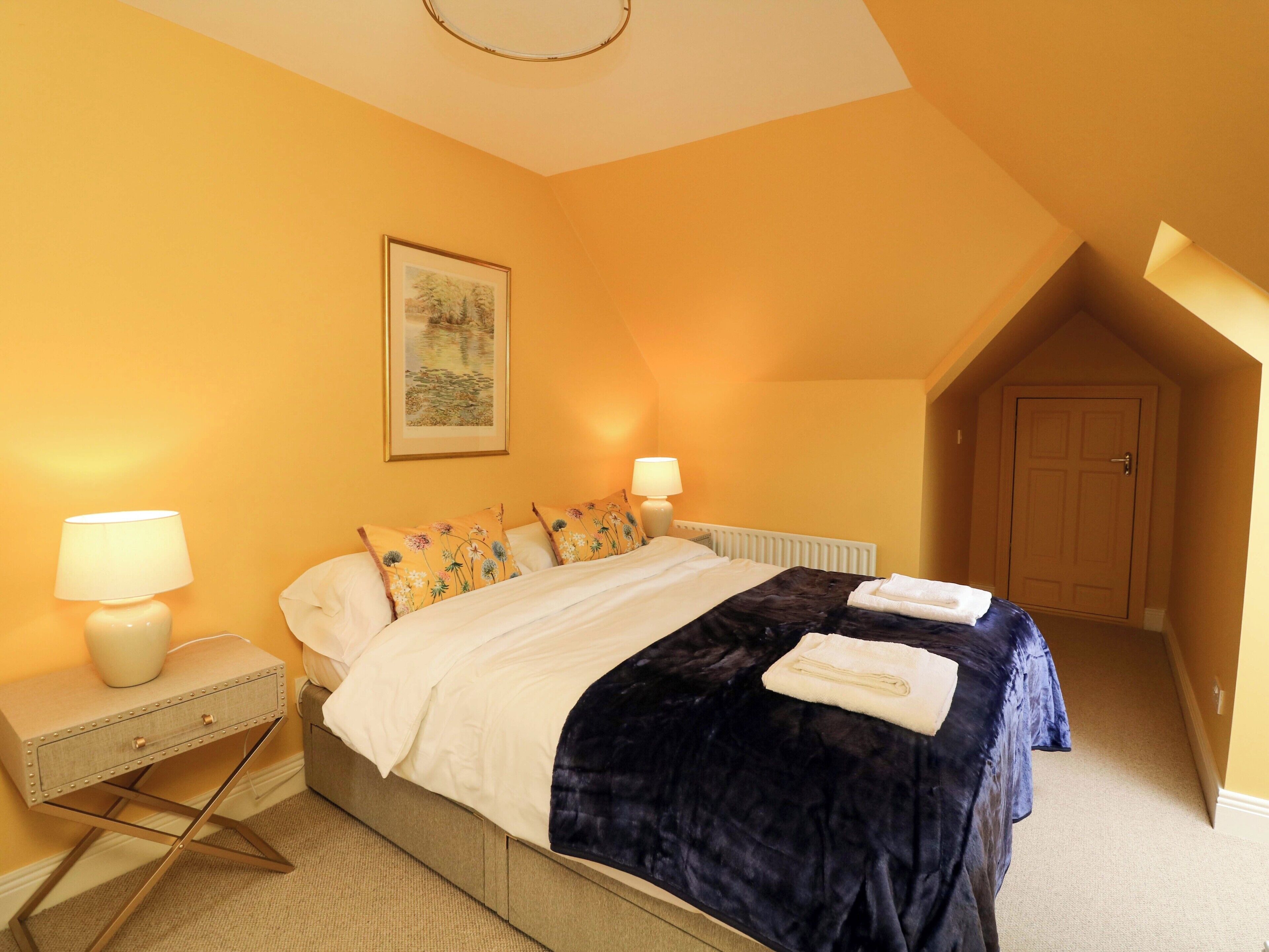 A bedroom with a bed, two bedside lamps, a radiator, a door, and a painting on the wall.