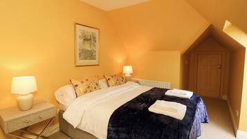 A bedroom with a bed, two bedside lamps, a radiator, a door, and a painting on the wall.
