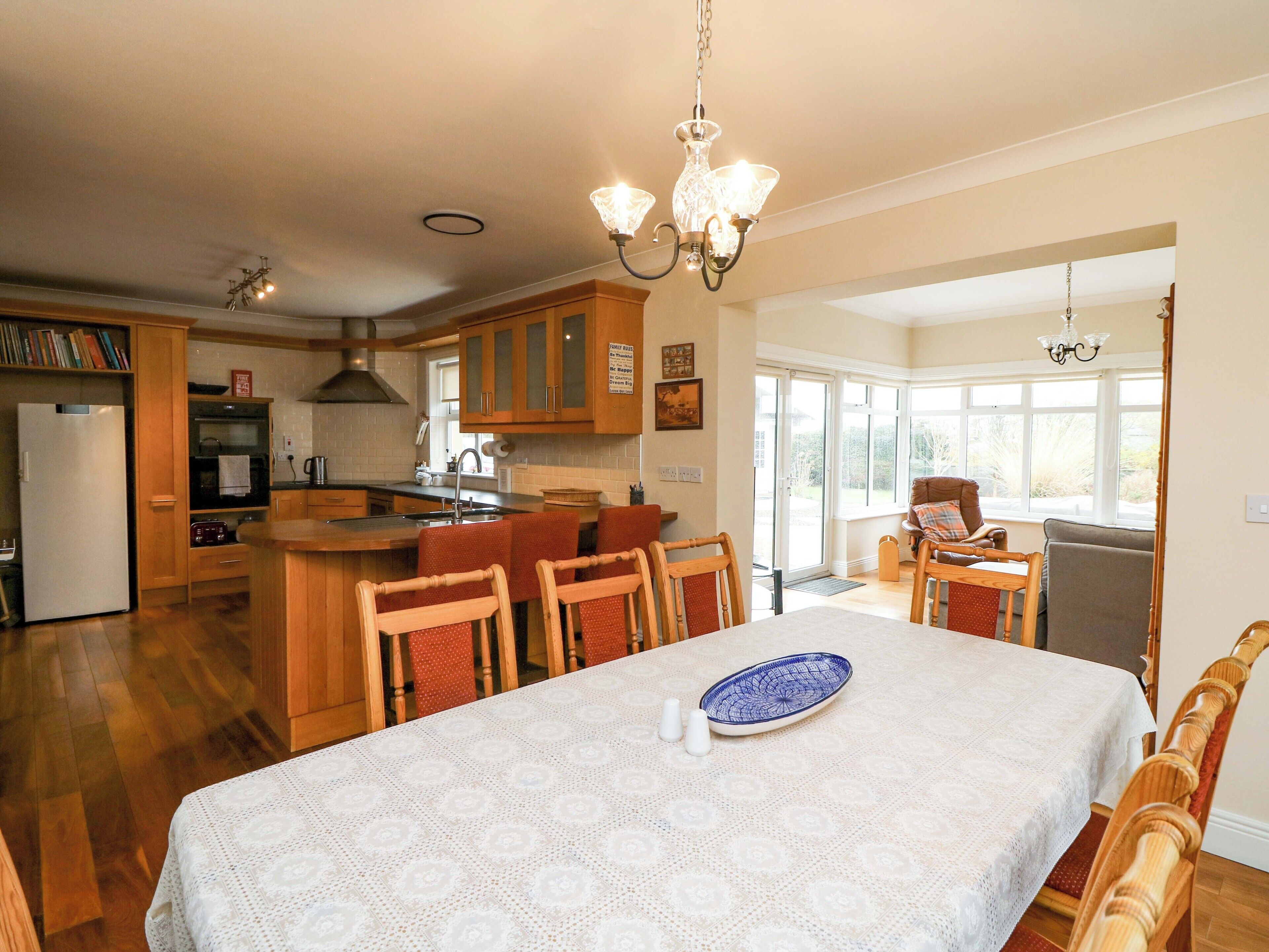 A spacious kitchen with wooden cabinets, a dining table with a lace tablecloth, and a chandelier.