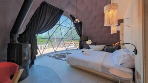 Une chambre moderne aménagée comme une tente, avec un lit, une petite table, une chaise rouge, un radiateur et une vue sur l’extérieur.