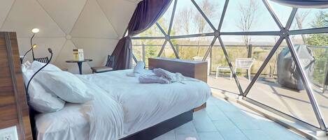A modern bedroom with a large bed, a bedside table, a lamp, and a view through large windows.