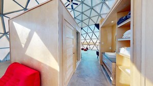 Un couloir d’hôtel avec un plafond au design géométrique, des murs en bois et une chaise rouge.