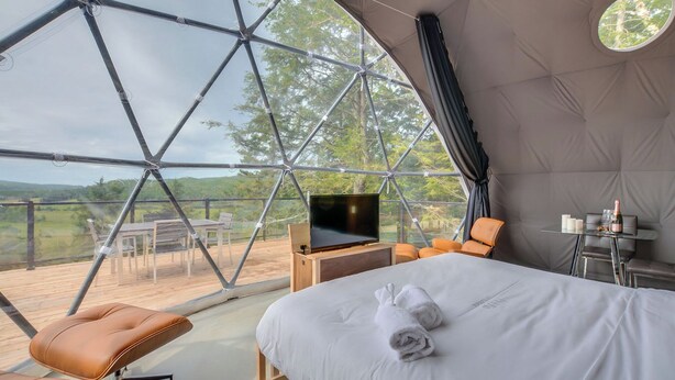 A modern tent-style room with a bed, seating area, and a TV.