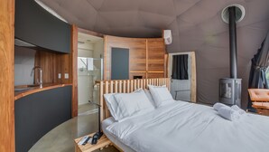 A modern hotel room with a bed, a wooden headboard, a small table, a desk, and a built-in heater.