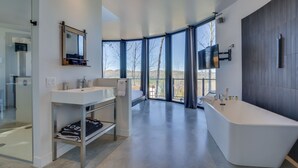 A modern bathroom with a large bathtub, a vanity with a mirror, and a shower area. - Bel Air Tremblant ROUND LOFT : 1 LIT KING, JACUZZI ET SAUNA (La Conception)