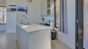 A modern bathroom with a white sink, a mirror, and a window with curtains. - Bel Air Tremblant ROUND LOFT : 1 LIT KING, JACUZZI ET SAUNA (La Conception)