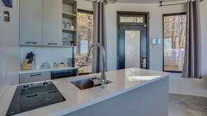 A modern kitchen with a built-in island, stainless steel appliances, and a large window with curtains. - Bel Air Tremblant ROUND LOFT : 1 LIT KING, JACUZZI ET SAUNA (La Conception)