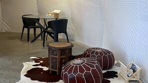 A room with a round wooden table, two black chairs, a decorative stool, and a large, round, dark-colored ottoman.