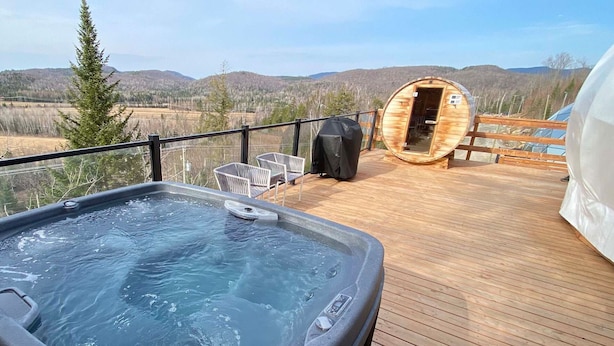 A hot tub on a wooden deck with a view of mountains and a sauna.