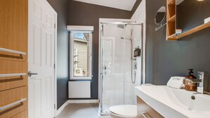 Een moderne badkamer met een douchecabine van glas, een wit toilet en een houten wastafelmeubel met spiegel.
