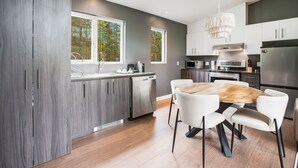 Een moderne keuken met een houten eettafel, witte stoelen en een kroonluchter.