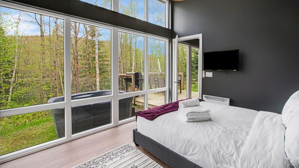 Een slaapkamer met een groot raam, een bed, een televisie en een balkon met een barbecue.
