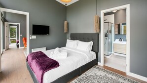 Een moderne slaapkamer met een groot bed, een televisie en een badkamer zichtbaar door een geopende deur.