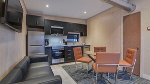 Une cuisine compacte dotée d’appareils électroménagers modernes, un coin salon avec un canapé et des fauteuils, et une petite table à manger.