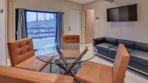 Une pièce moderne avec une table en verre, des fauteuils en cuir, un canapé et un téléviseur fixé au mur.