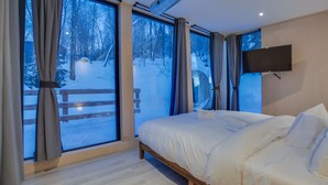 Une chambre avec une grande fenêtre, un lit et un téléviseur fixé au mur.