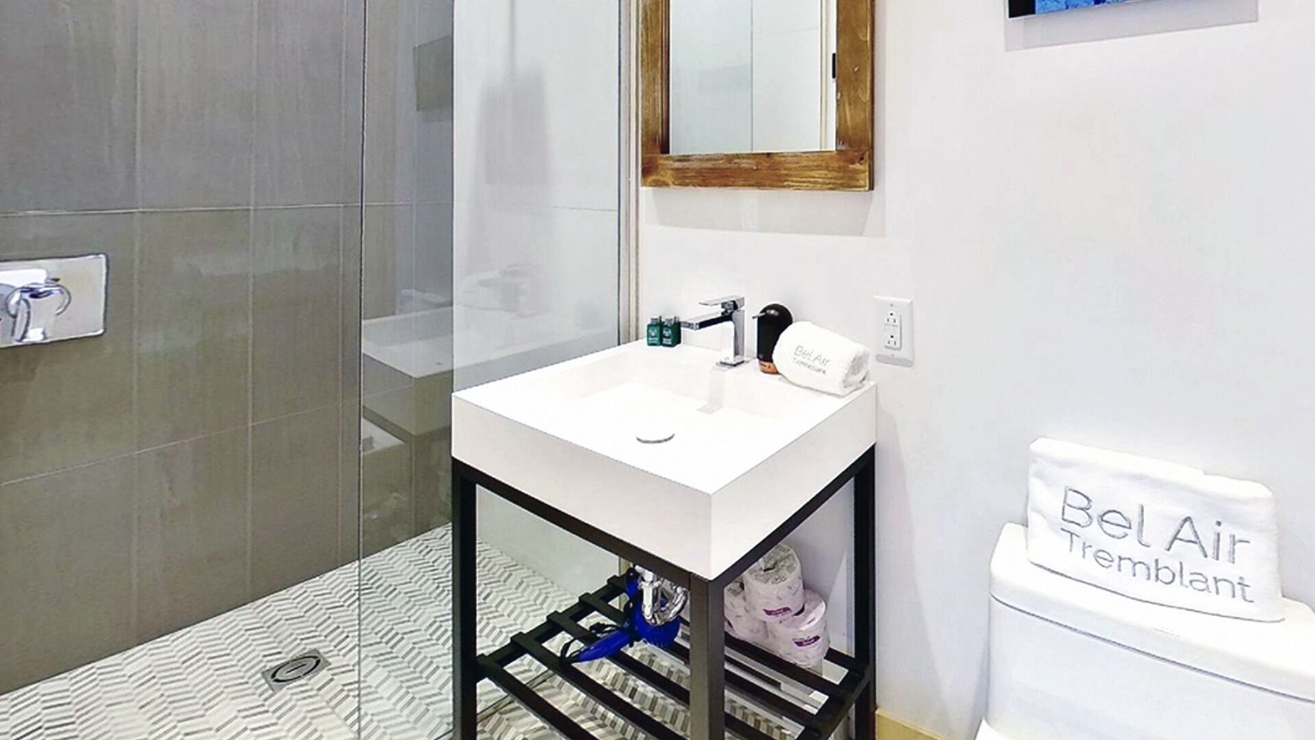 A bathroom with a white sink, a mirror, a toilet labeled 'Bel-Air Tremblant,' and a shower area.