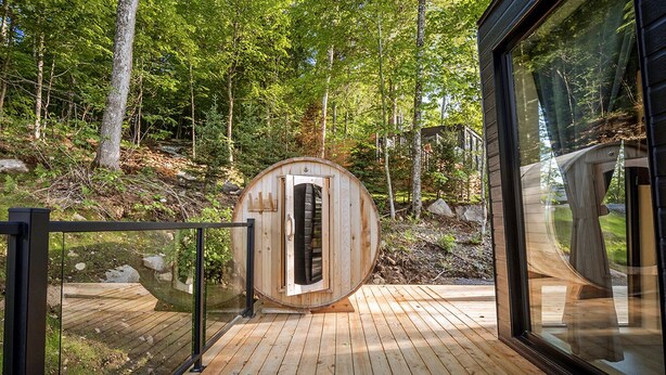 Une structure de sauna en bois dotée d’une porte en verre, entourée d’une terrasse en bois et d’une forêt.