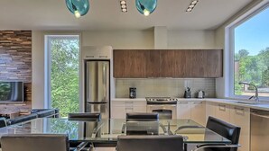 A modern kitchen with a glass dining table, stainless steel appliances, and wooden cabinets.