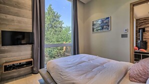 A bedroom with a large window, a bed, a mounted TV, and a wall-mounted heater.