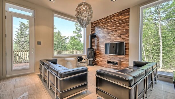 A modern living room with a fireplace, a large TV, and a balcony with a view of trees.
