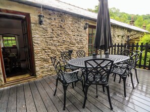 Ein Steinhaus mit Holzterrasse, Sitzgelegenheiten im Freien und Blick auf Grünflächen.