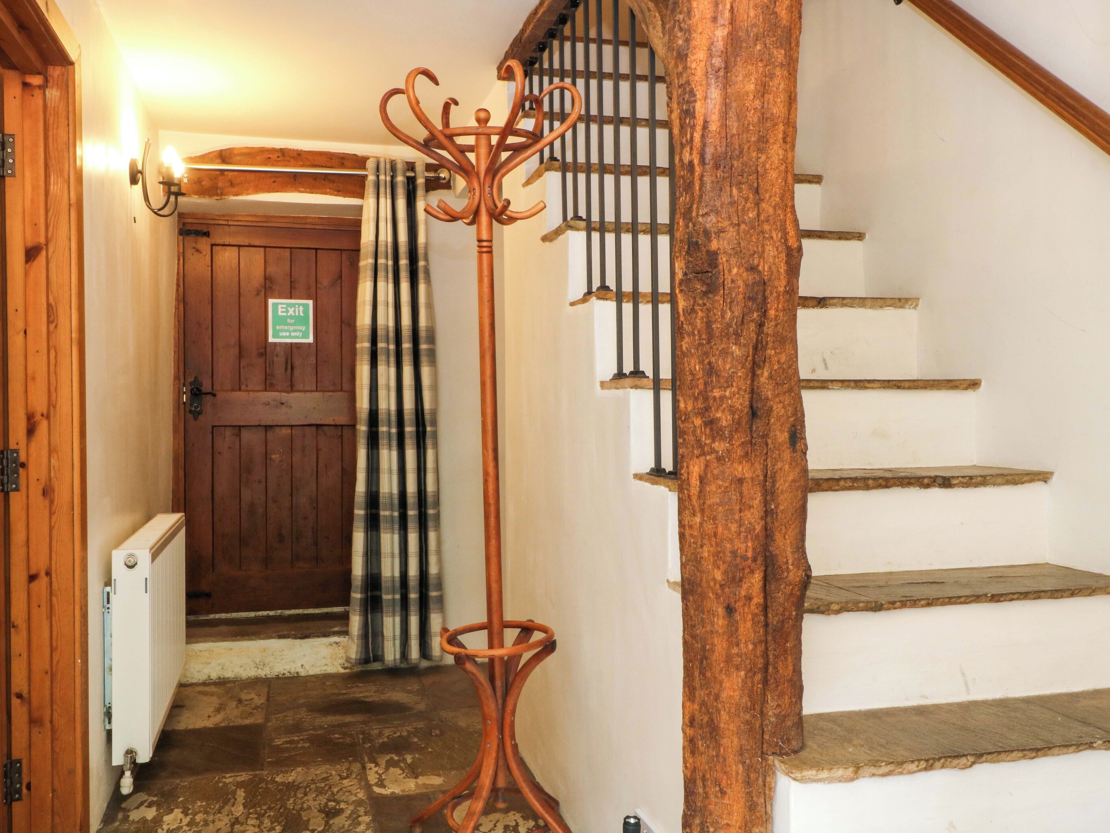 A wooden staircase with a rustic design, a coat rack, a plaid curtain, and a door with an emergency exit sign.