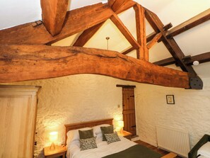 Un dormitorio con vigas de madera a la vista, una cama con dos almohadas, una mesita de noche con una lámpara y un radiador blanco.