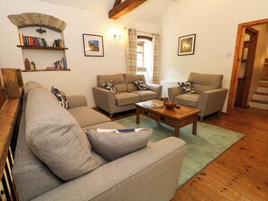 Ein Wohnzimmer mit einer Couch, zwei Sesseln, einem Couchtisch, einem Bücherregal und einem Fenster mit Vorhängen.