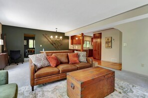 A living room with a brown leather sofa, a wooden coffee table, and a dining area with wooden cabinets and a chandelier. - Stratton; 8 min. Swimming; 2 min. Pet Friendly (Winhall)