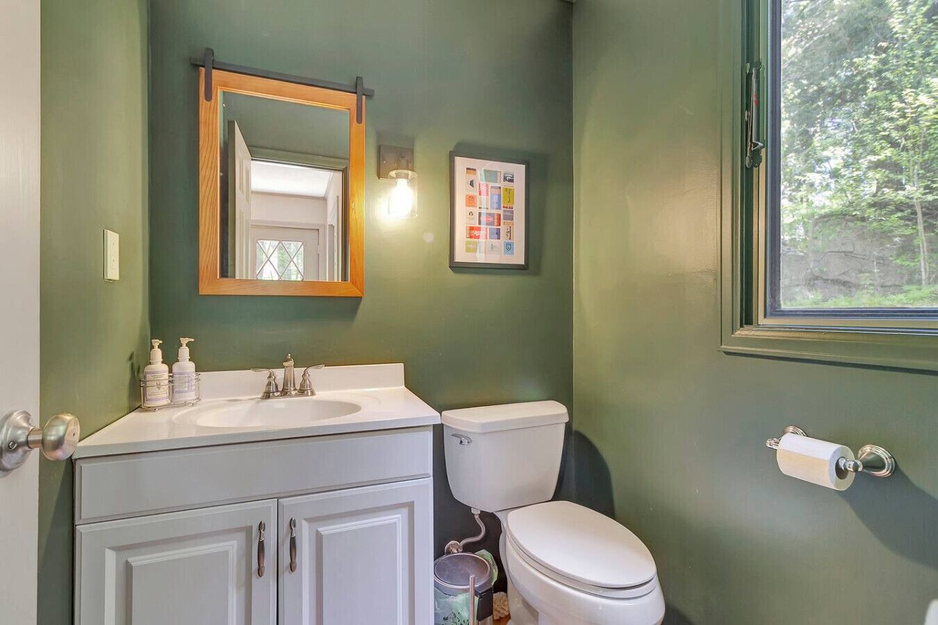 A bathroom with a white sink, a toilet, a mirror, and a window.