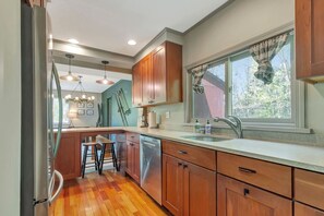 A kitchen with wooden cabinets, a stainless steel refrigerator, a sink, and a window with curtains. - Stratton; 8 min. Swimming; 2 min. Pet Friendly (Winhall)