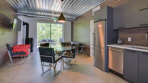 A modern kitchen with stainless steel appliances, a dining area with a glass table and chairs, and a view through large windows. - Bel Air Tremblant ANDORRA: 2 CHAMBRES, JACUZZI (La Conception)