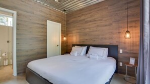 A modern bedroom with a wooden wall, a bed with white linens, a bedside table, and a hanging light fixture. - Bel Air Tremblant ANDORRA: 2 CHAMBRES, JACUZZI (La Conception)