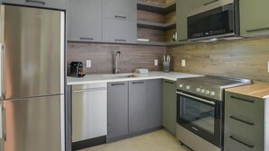 A modern kitchen with stainless steel appliances, grey cabinetry, and a wooden backsplash. - Bel Air Tremblant ANDORRA: 2 CHAMBRES, JACUZZI (La Conception)