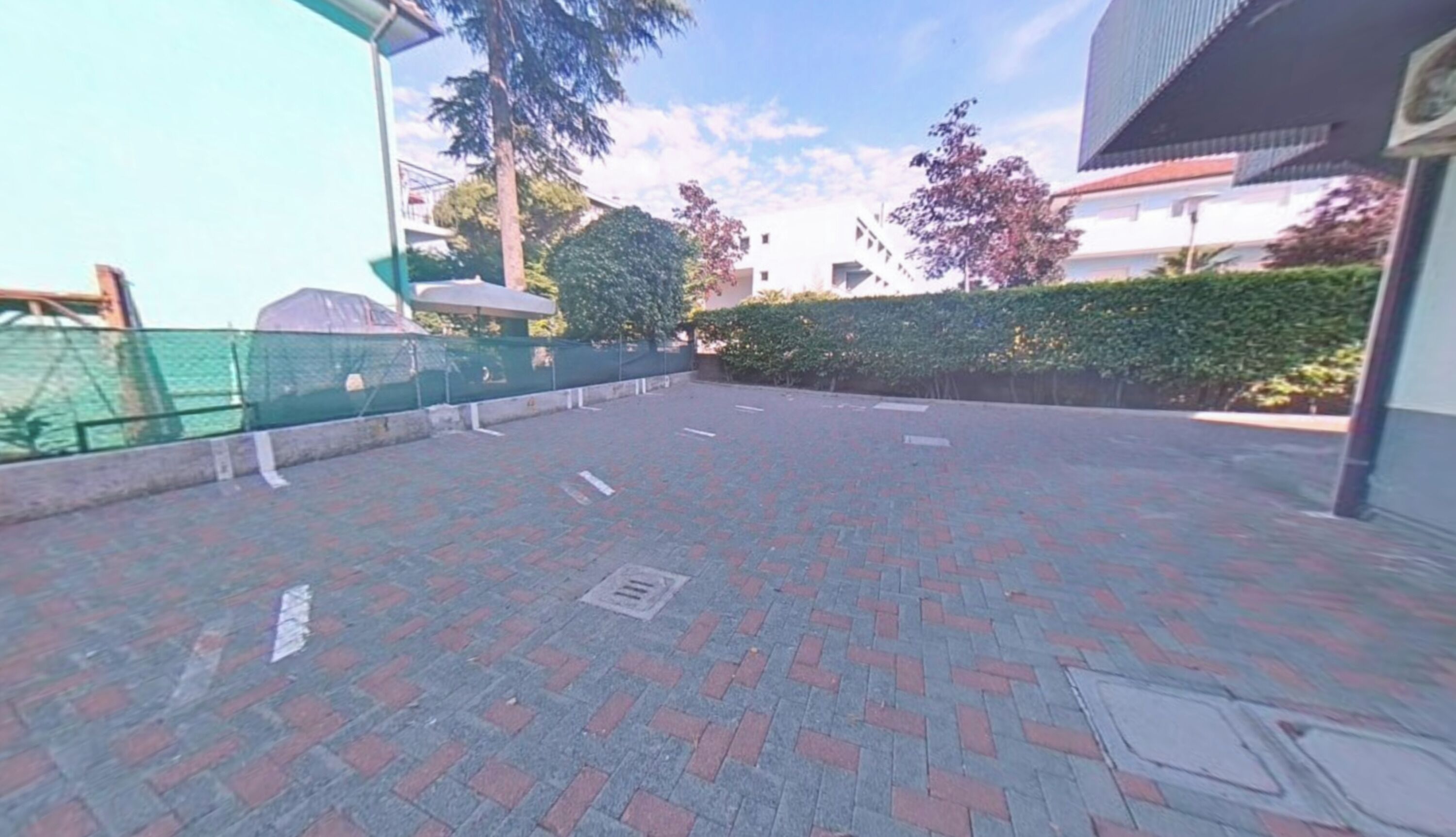 An outdoor paved area with a fence, trees, and a building in the background.