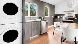 Una cocina moderna con electrodomésticos integrados, un comedor con mesa redonda y un área de lavandería con lavadoras apiladas.