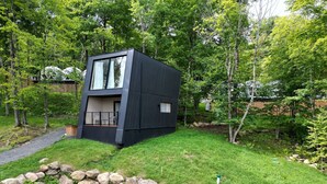 Una cabaña moderna de dos pisos con balcón, rodeada de un paisaje natural.