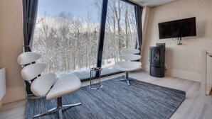 Una habitación moderna con un amplio ventanal, chimenea y televisor montado en la pared.