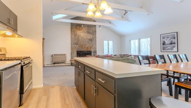 A modern kitchen with a stone fireplace, a dining area with a large table, and a loft-style ceiling with skylights. - Stratton; walk on/off, shuttle Rt, pool table, shuffle puck, darts, dogs OK (Winhall)