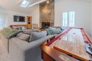 A living room with a pool table, a stone fireplace, a sofa, and a television.