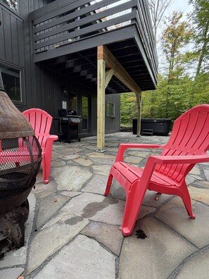 Een terras met twee rode Adirondack-stoelen, een barbecue en een vloer van stenen tegels.
